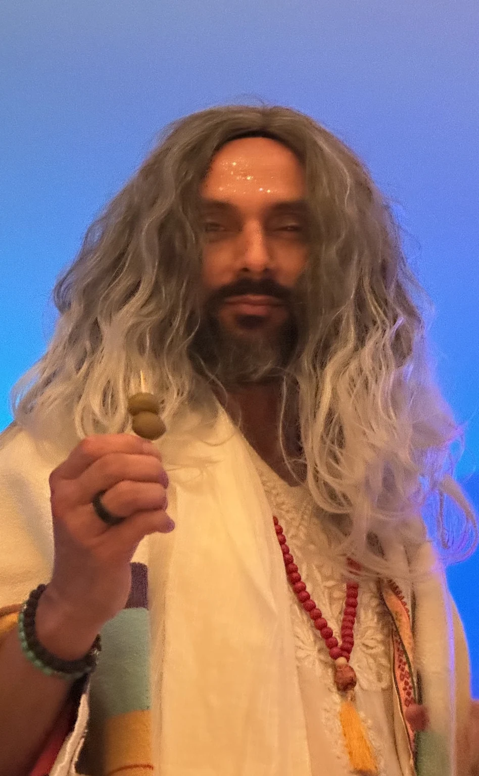 Raja Beta, silver-haired and dressed in ceremonial white, raising two olives
